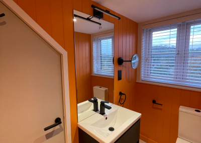 Newly decorated bathroom with bright orange woodwork, a new dark wood sink area and white toilet and sink.