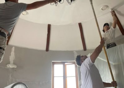 3 decorators working inside a round room, painting high ceilings with an elaborate candelabra lamp