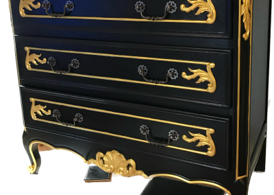 Black chest of drawers with gold scroll detailing.