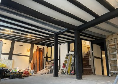 A large room with dark stained wooden beams, dusty floors covered with decorating materials.