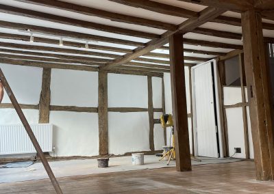 A room in the process of renovation. Wooden beams have been stripped to their original oak colour and the floor is dusty with a broom.