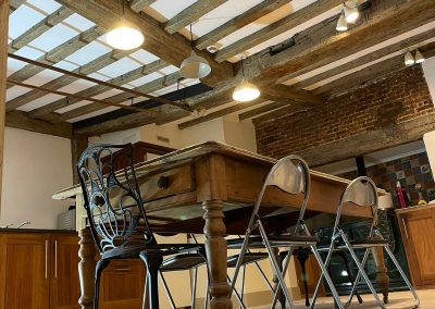 A large kitchen area with newly renovated wooden beams along the ceiling. There is a large inglenook fireplace with traditional aga oven.